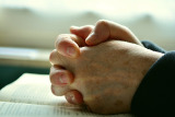 Hands clasped in prayer resting on the bible.